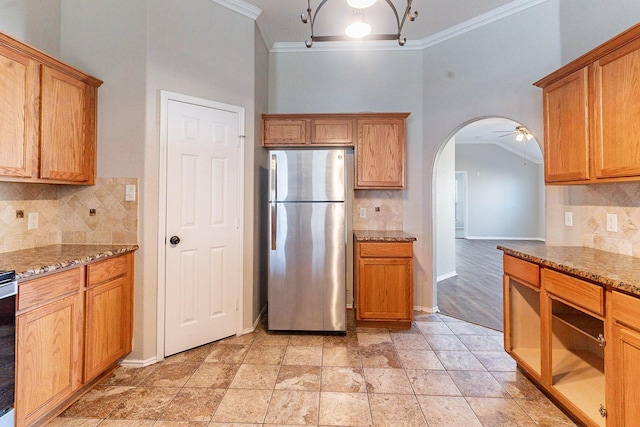 kitchen featuring stainless steel refrigerator, crown molding, ceiling fan, decorative backsplash, and stone countertops