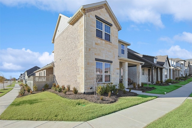 view of side of home featuring stone siding, a residential view, a lawn, and brick siding