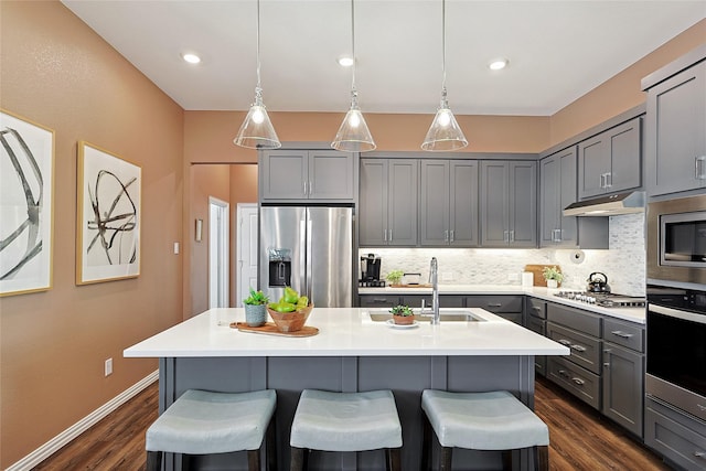 kitchen with tasteful backsplash, stainless steel appliances, gray cabinets, and an island with sink