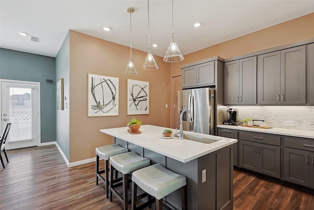 kitchen featuring gray cabinetry, stainless steel fridge with ice dispenser, an island with sink, pendant lighting, and sink