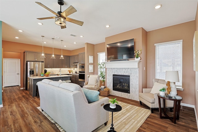 living room with dark wood-type flooring, a tiled fireplace, ceiling fan, and sink