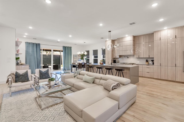 living room featuring sink, a notable chandelier, and light hardwood / wood-style flooring