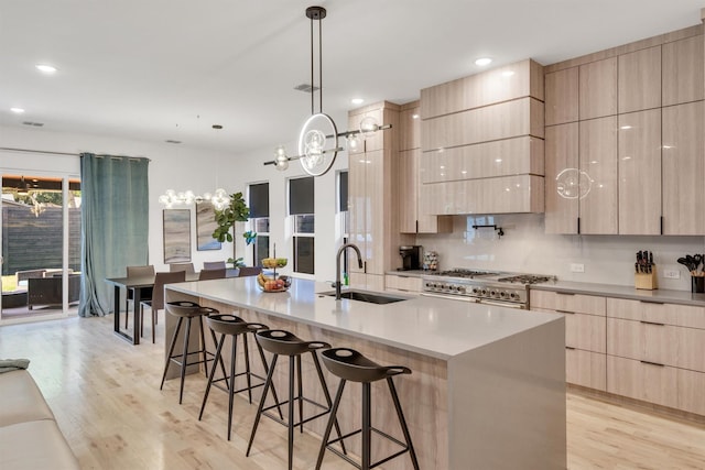 kitchen featuring range with two ovens, a center island with sink, light brown cabinetry, a kitchen bar, and sink