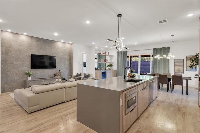 kitchen with sink, decorative light fixtures, light hardwood / wood-style floors, a large island with sink, and appliances with stainless steel finishes