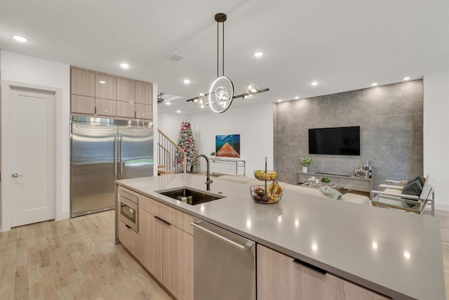 kitchen with built in appliances, decorative light fixtures, light hardwood / wood-style floors, light brown cabinets, and sink