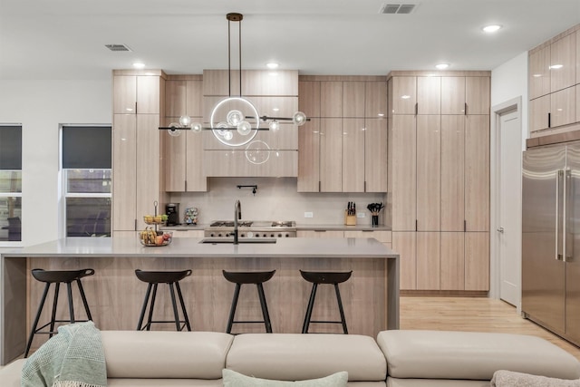 kitchen with stainless steel built in fridge, pendant lighting, light brown cabinetry, a center island with sink, and a breakfast bar