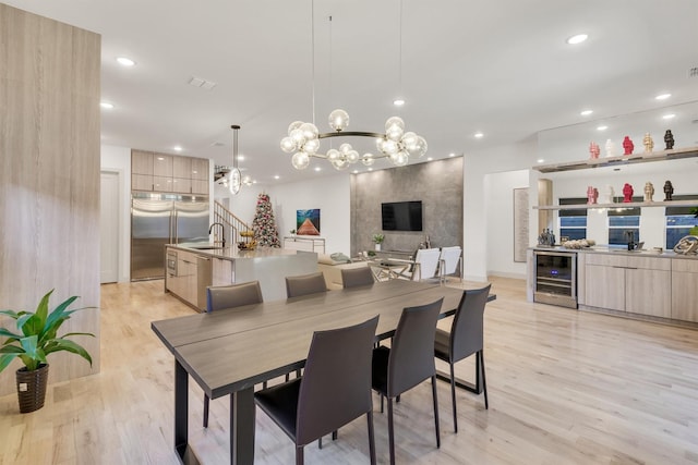 dining room with sink, a notable chandelier, beverage cooler, and light hardwood / wood-style floors