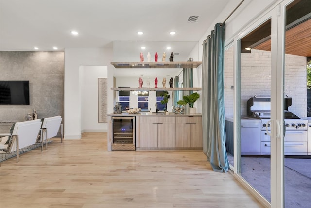 bar featuring sink, beverage cooler, light wood-type flooring, and light brown cabinetry