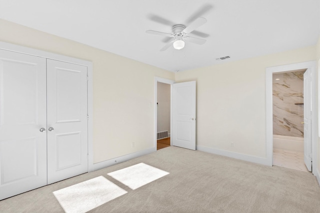 unfurnished bedroom featuring light carpet, ensuite bath, a closet, and ceiling fan