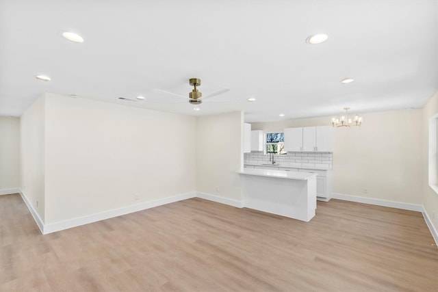 unfurnished living room featuring sink, light hardwood / wood-style flooring, and ceiling fan with notable chandelier