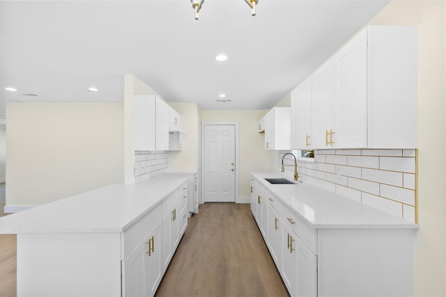 kitchen with kitchen peninsula, light hardwood / wood-style flooring, backsplash, white cabinets, and sink