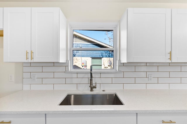 kitchen with sink, white cabinets, tasteful backsplash, and light stone counters