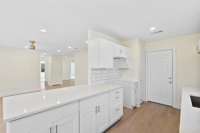 kitchen with light hardwood / wood-style floors, white cabinetry, light stone counters, and tasteful backsplash