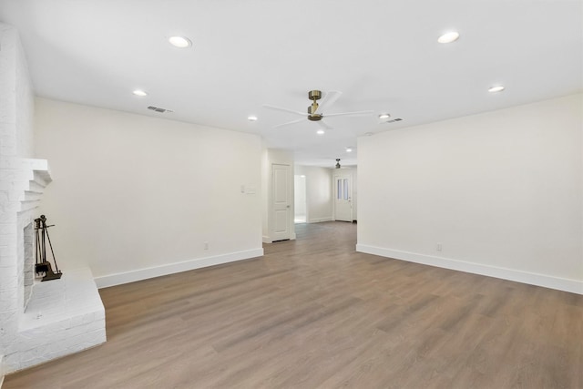 unfurnished living room featuring wood-type flooring, a brick fireplace, and ceiling fan