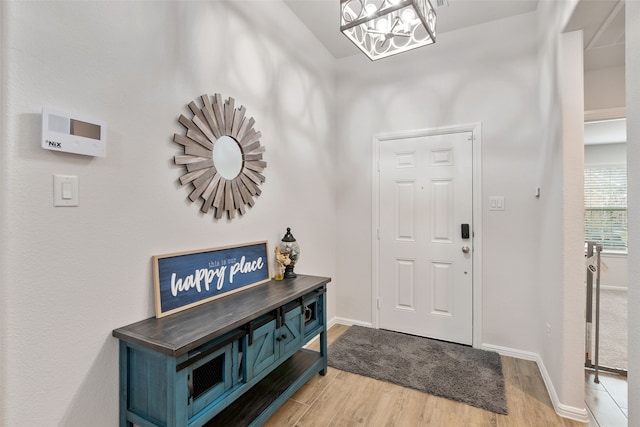 foyer entrance with light wood-style flooring, baseboards, and an inviting chandelier