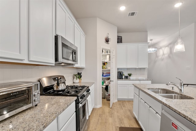 kitchen with appliances with stainless steel finishes, white cabinets, a sink, and backsplash