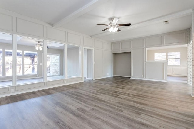 unfurnished living room with beamed ceiling, ceiling fan, a wealth of natural light, and hardwood / wood-style floors