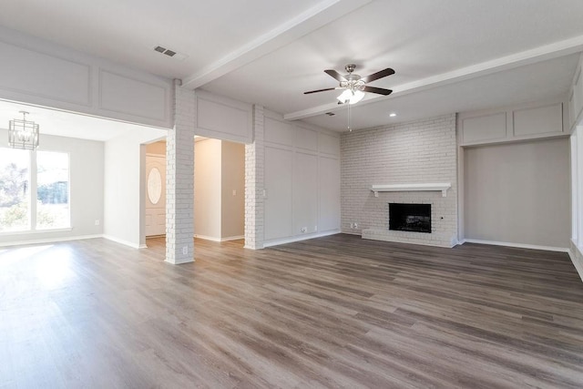 unfurnished living room featuring a fireplace, beamed ceiling, ornate columns, hardwood / wood-style floors, and ceiling fan