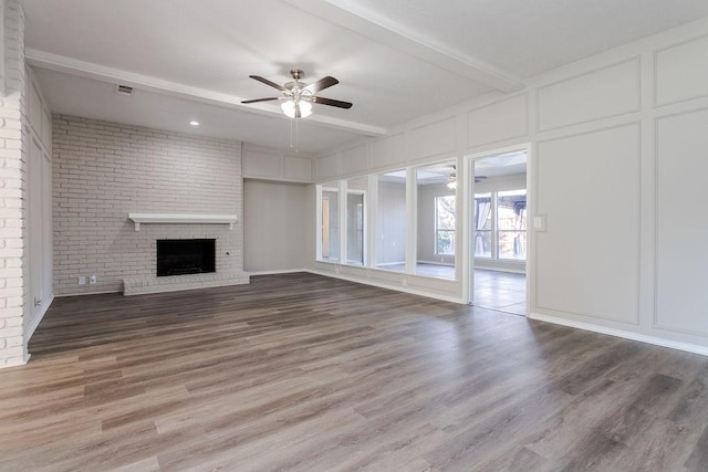 unfurnished living room with beamed ceiling, ceiling fan, wood-type flooring, a brick fireplace, and brick wall