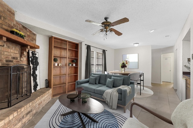 tiled living room featuring a brick fireplace, a textured ceiling, and ceiling fan