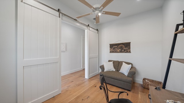 living area featuring light hardwood / wood-style floors, ceiling fan, and a barn door