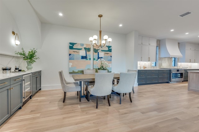 dining space with beverage cooler, a chandelier, and light wood-type flooring