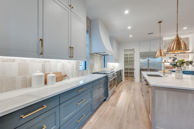 kitchen with light stone countertops, hanging light fixtures, high end range, custom range hood, and sink