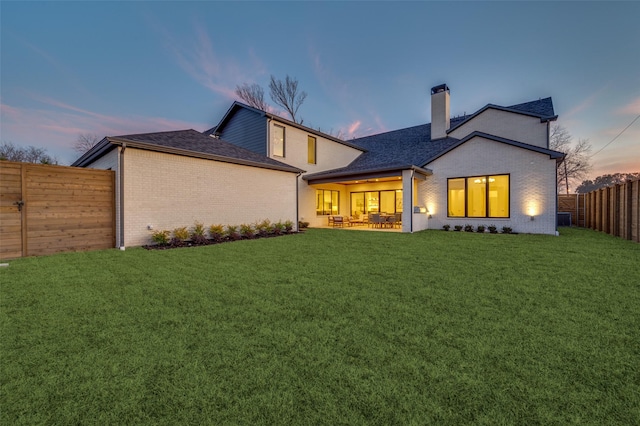 back house at dusk with a lawn and a patio