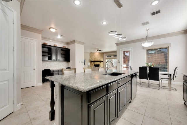 kitchen featuring sink, stainless steel dishwasher, light stone countertops, a center island with sink, and pendant lighting