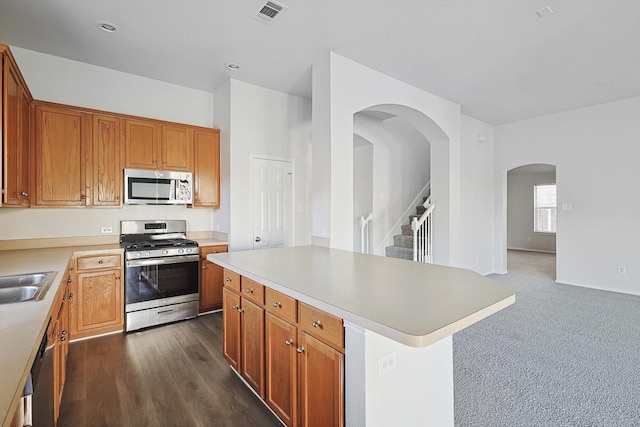 kitchen with appliances with stainless steel finishes, a center island, sink, and dark carpet