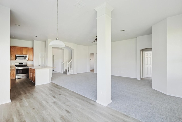 kitchen with stainless steel appliances, a center island, ceiling fan, hanging light fixtures, and light colored carpet