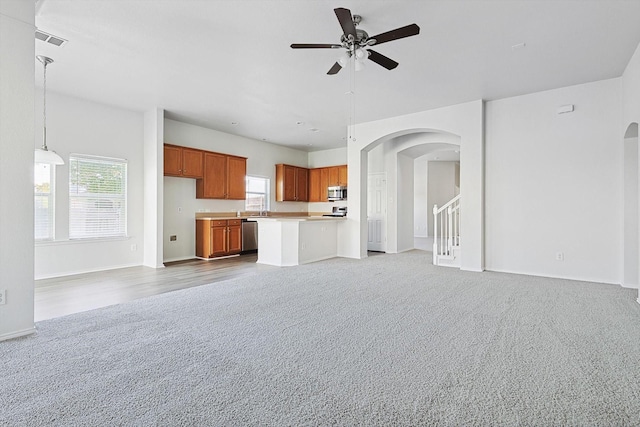 unfurnished living room featuring light colored carpet, ceiling fan, and a wealth of natural light