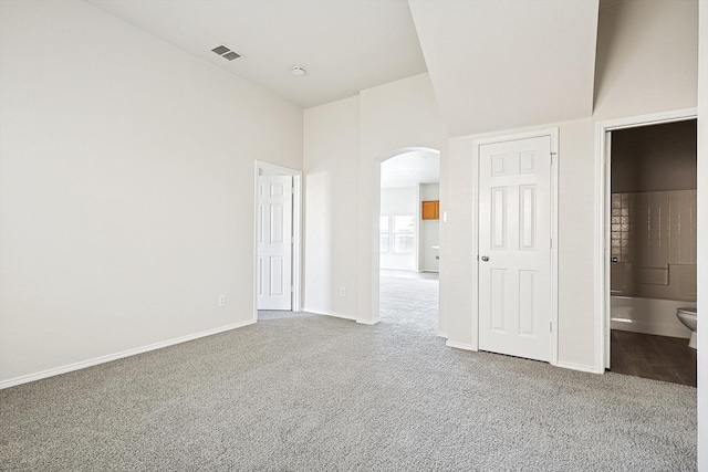 unfurnished bedroom featuring a high ceiling, ensuite bath, and carpet