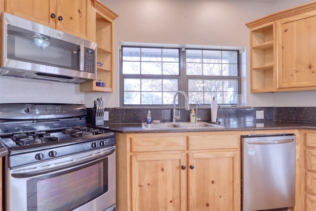 kitchen with sink, stainless steel appliances, dark stone counters, and light brown cabinetry