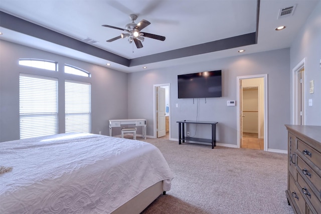 carpeted bedroom featuring ensuite bathroom, ceiling fan, and a tray ceiling