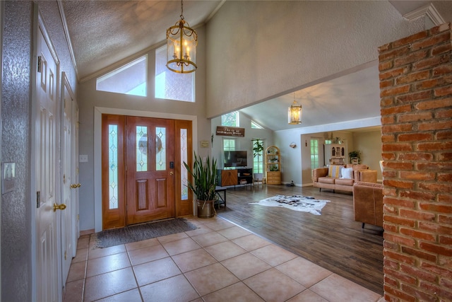 entryway featuring a textured ceiling, high vaulted ceiling, an inviting chandelier, and light tile patterned floors