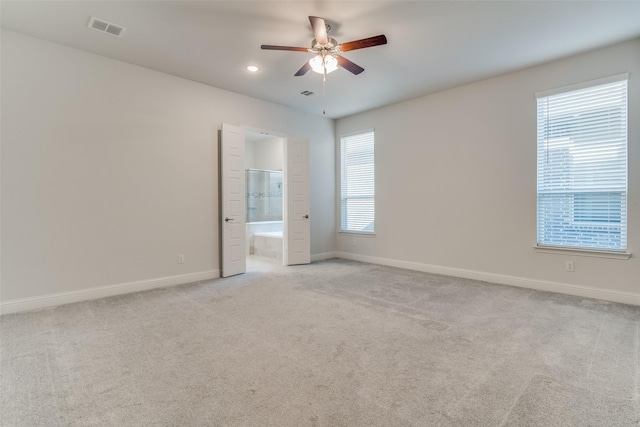 unfurnished bedroom featuring ensuite bath, ceiling fan, multiple windows, and light colored carpet