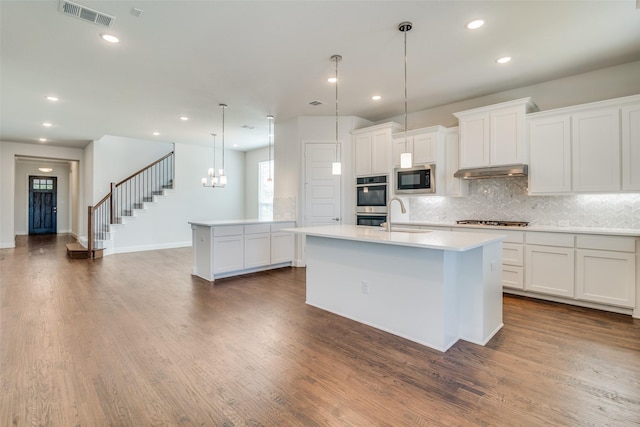 kitchen with dark wood-type flooring, pendant lighting, stainless steel appliances, an island with sink, and white cabinetry