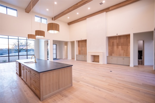 kitchen with a large fireplace, an island with sink, a towering ceiling, sink, and decorative light fixtures