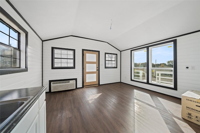 unfurnished living room featuring an AC wall unit, wooden walls, sink, and vaulted ceiling