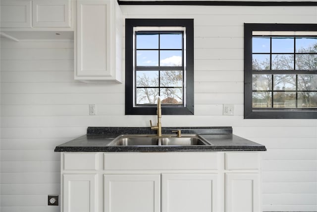 kitchen featuring sink, white cabinetry, and wooden walls