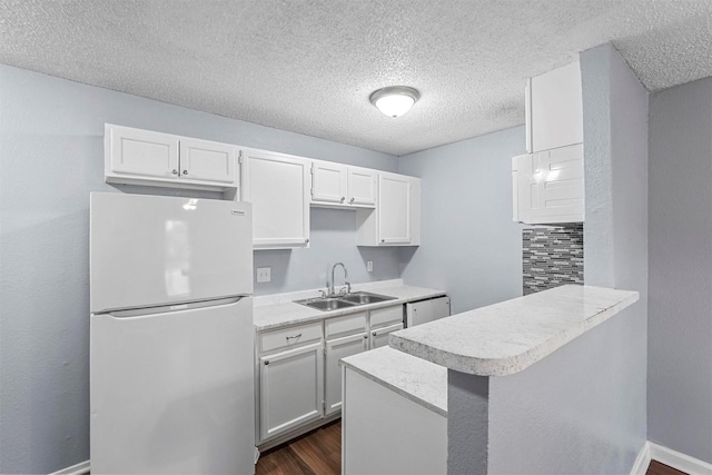 kitchen with white refrigerator, sink, white cabinetry, kitchen peninsula, and backsplash