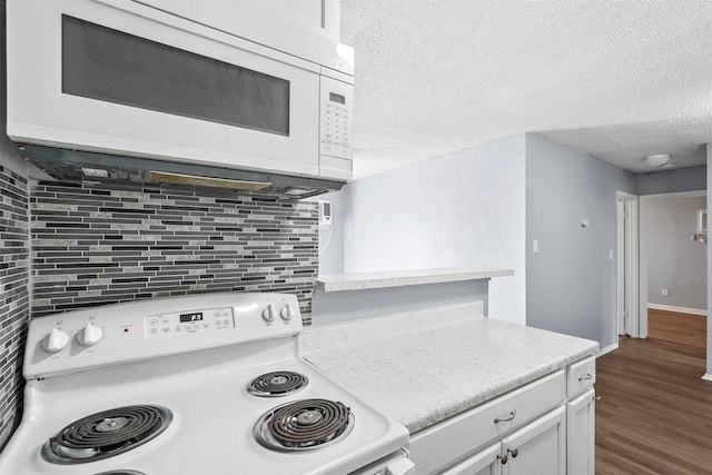 kitchen featuring white appliances, wood-type flooring, a textured ceiling, white cabinets, and tasteful backsplash