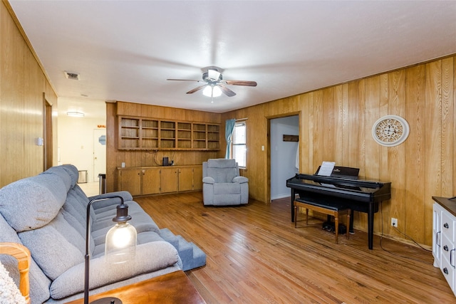 living room with wood walls, ceiling fan, and light wood-type flooring