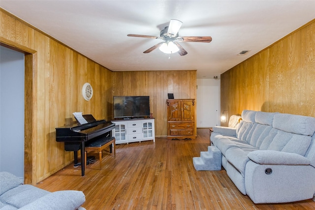 living room with hardwood / wood-style flooring, wood walls, and ceiling fan