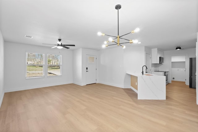 kitchen with hanging light fixtures, light wood-type flooring, kitchen peninsula, light stone counters, and white cabinets