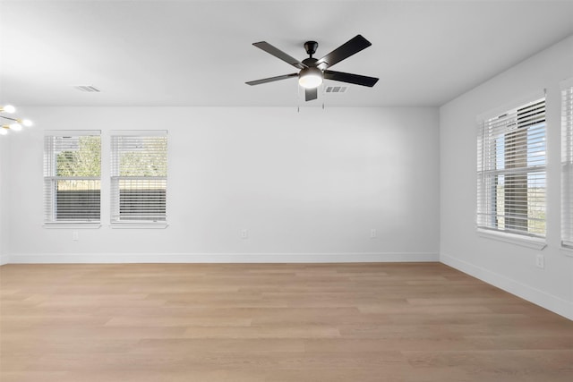 empty room with ceiling fan with notable chandelier and light hardwood / wood-style flooring