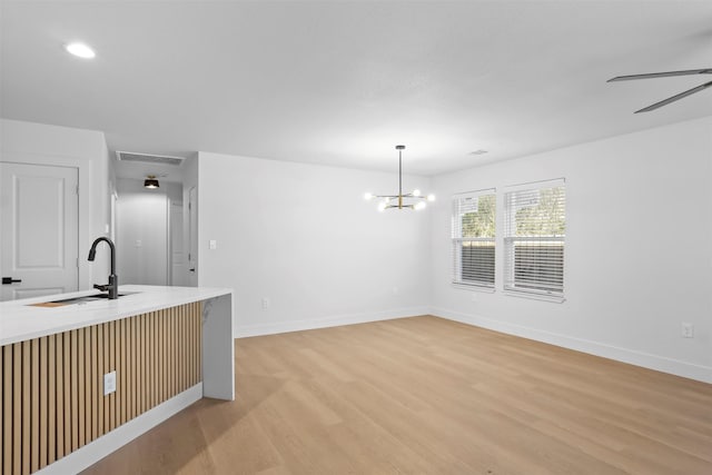 kitchen featuring sink, ceiling fan with notable chandelier, light wood-type flooring, and hanging light fixtures