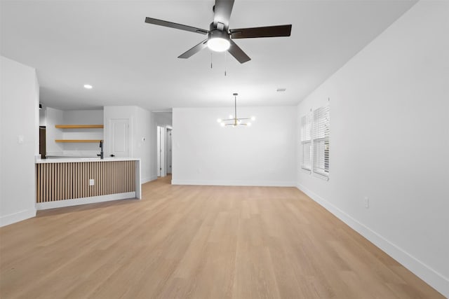 unfurnished living room with ceiling fan with notable chandelier and light hardwood / wood-style flooring