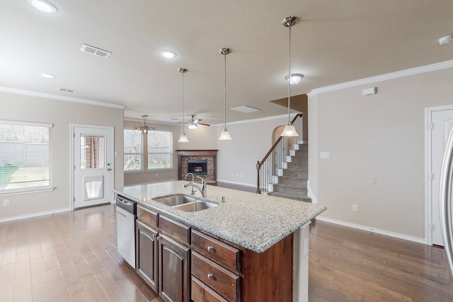 kitchen featuring sink, crown molding, a fireplace, an island with sink, and stainless steel dishwasher